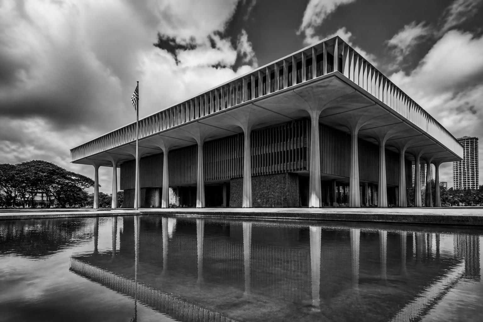 Black and white photo of the Hawaiʻi State Capitol building in Honolulu with dramatic sky and reflecting pool, the seat of the legislature that enacted Act 204