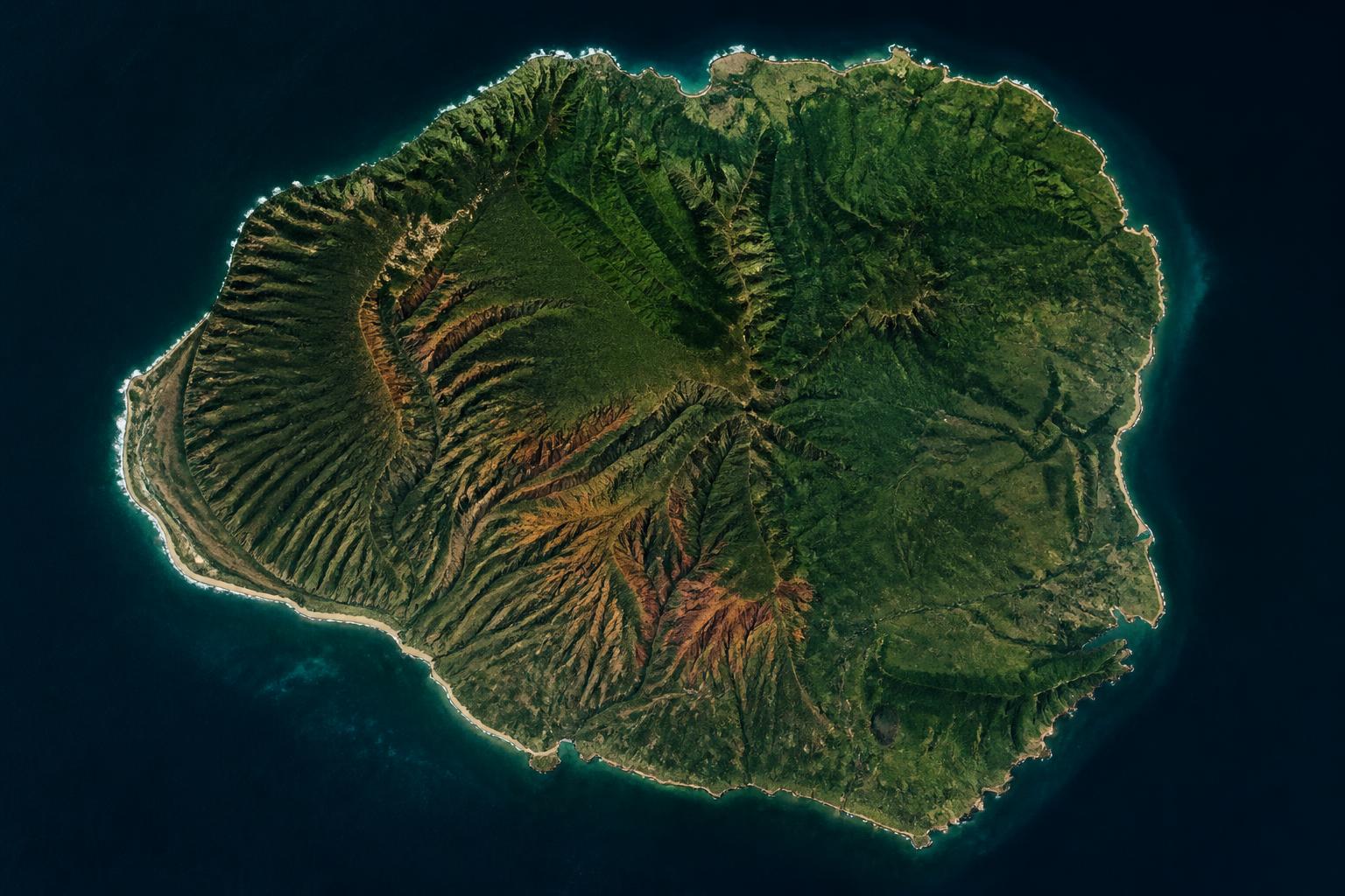 Aerial view of Kauaʻi, Hawaiʻi. Forested island surrounded by deep Pacific ocean.